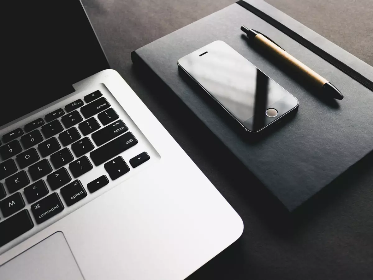 A laptop, a smartphone, a notebook and a pen on a dark surface.