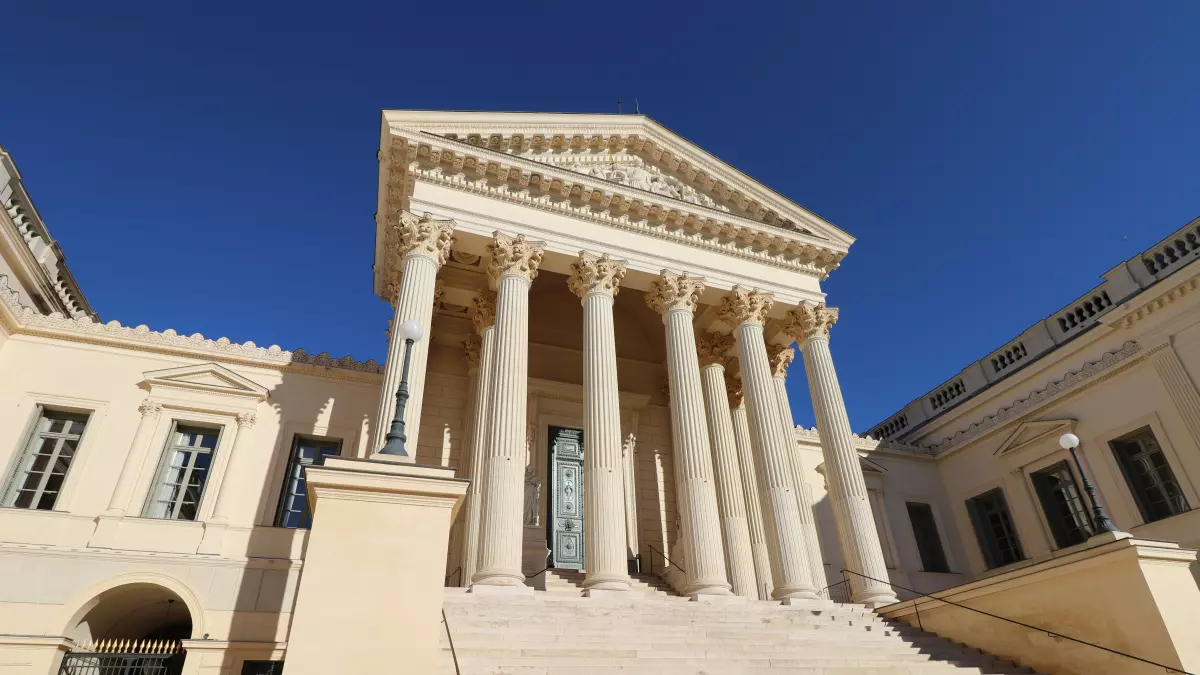 A low-angle shot of a classic courthouse with a columned facade and a staircase leading up to the entrance. The sky is clear blue.