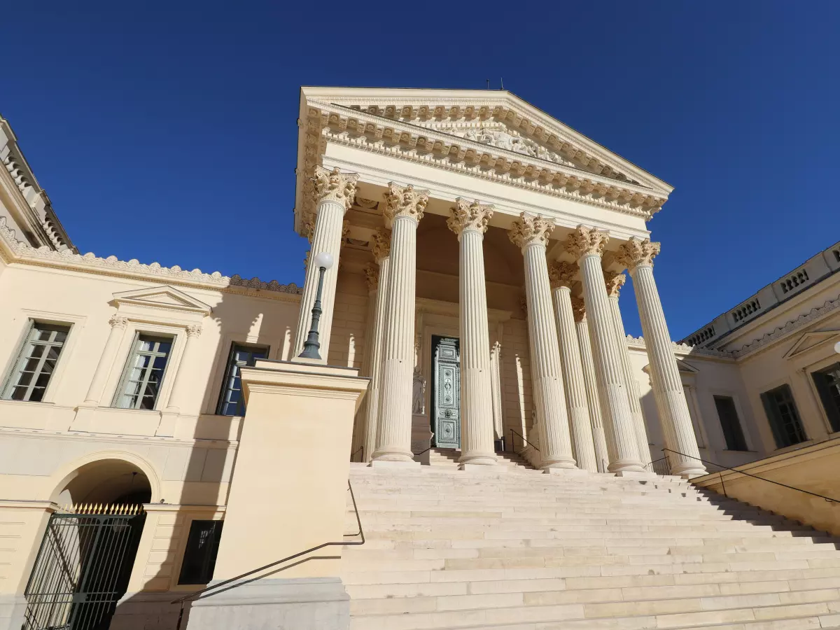 A low-angle shot of a classic courthouse with a columned facade and a staircase leading up to the entrance. The sky is clear blue.