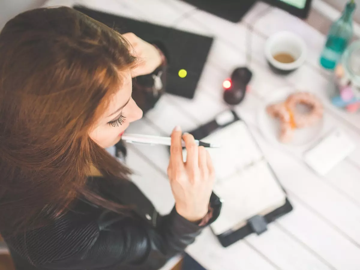 A woman sits at a desk, staring pensively at a notebook.