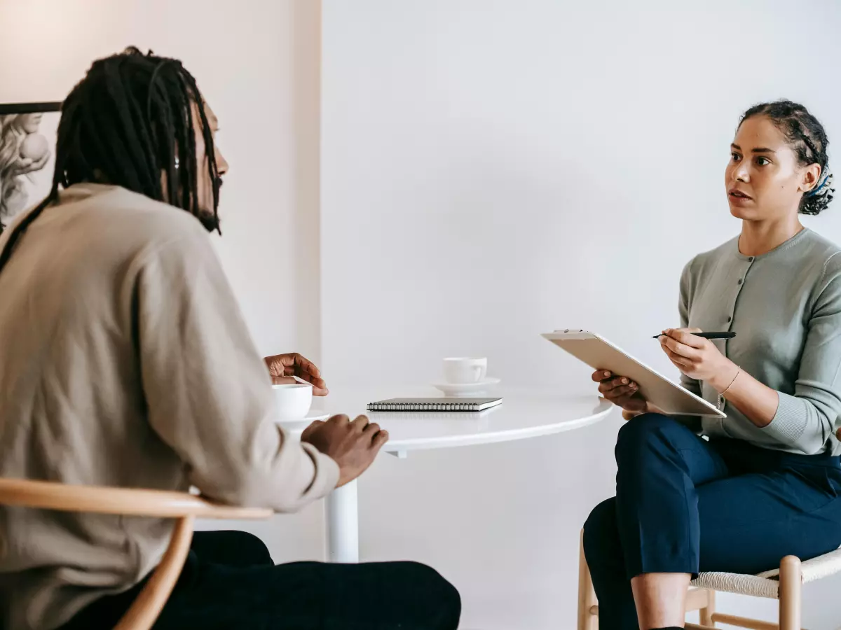 Two people, a man and a woman, are having a conversation in a business setting. The woman is holding a notepad and a pen in her hands.