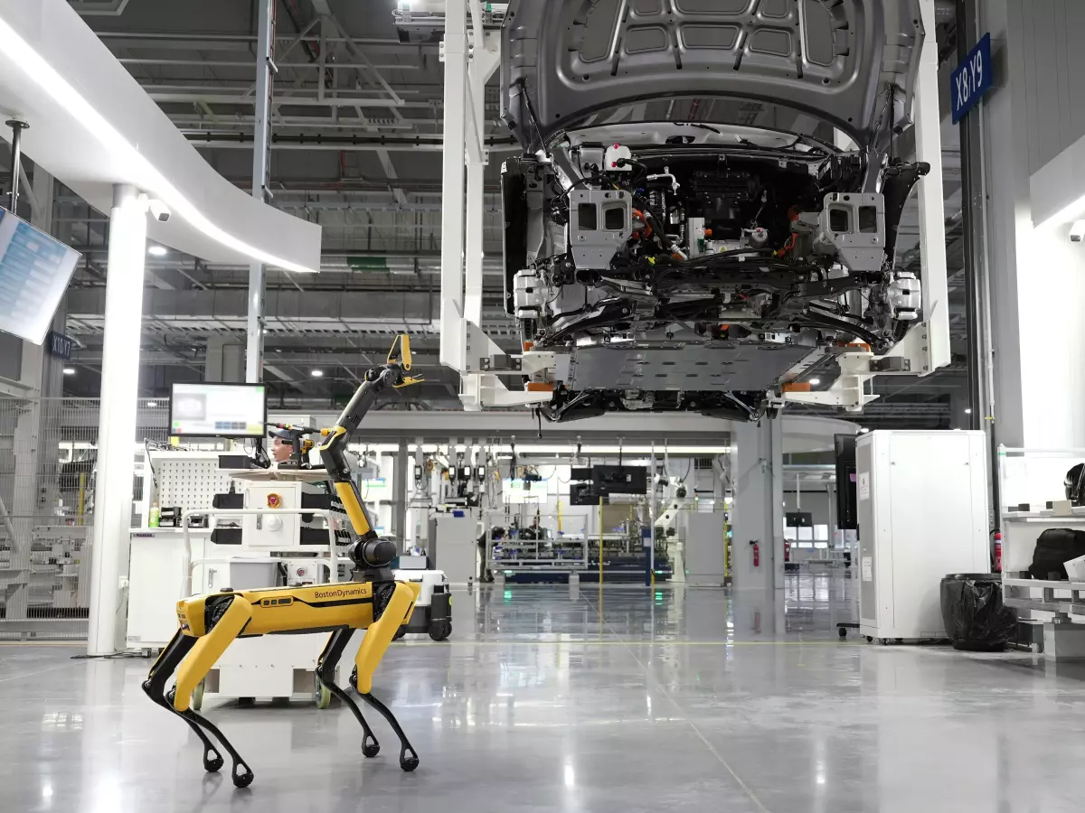 A yellow robotic dog with a robotic arm attached walks in a large warehouse.