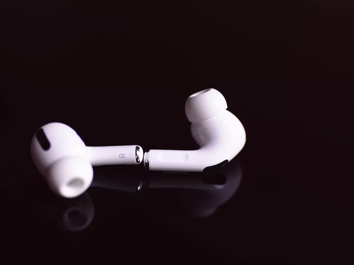 A single white AirPod earbud on a black surface, showcasing the lack of a physical button.