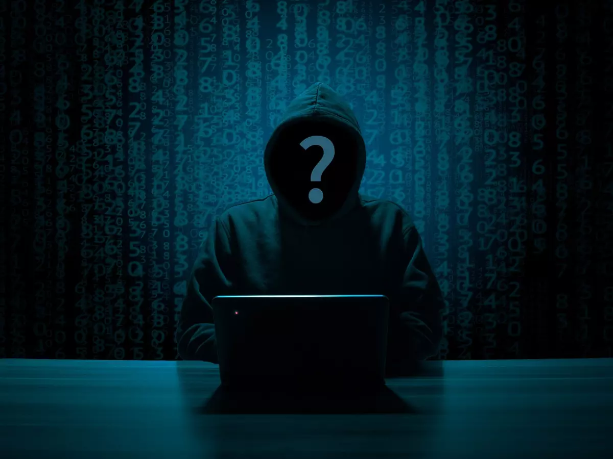 A hooded figure with a question mark over their face is sitting in front of a laptop, against a backdrop of binary code. The scene is dimly lit and conveys a sense of mystery and secrecy.