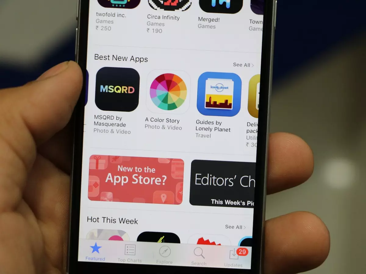 A person is holding a white smartphone, and the screen is showing the app store. The screen is zoomed in on a "Best New Apps" section of the app store.