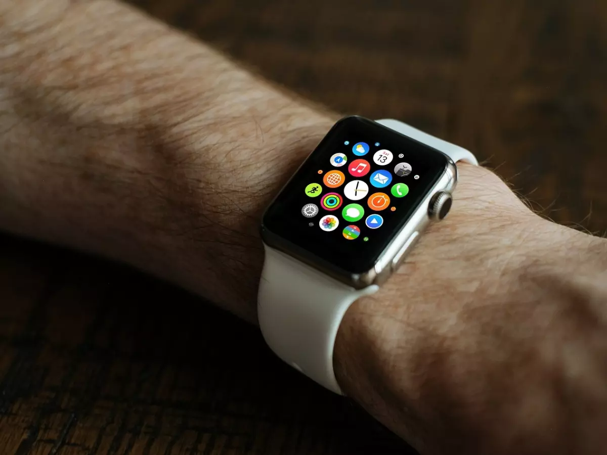 A white Apple Watch on a man's wrist, displaying various apps on the screen.