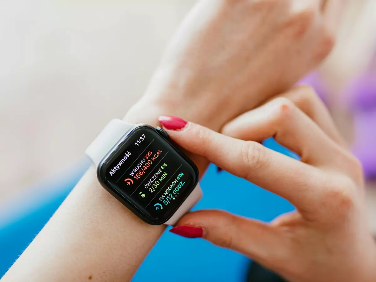 A woman wearing a white Apple Watch with a black band is interacting with it, her hand is touching the screen.