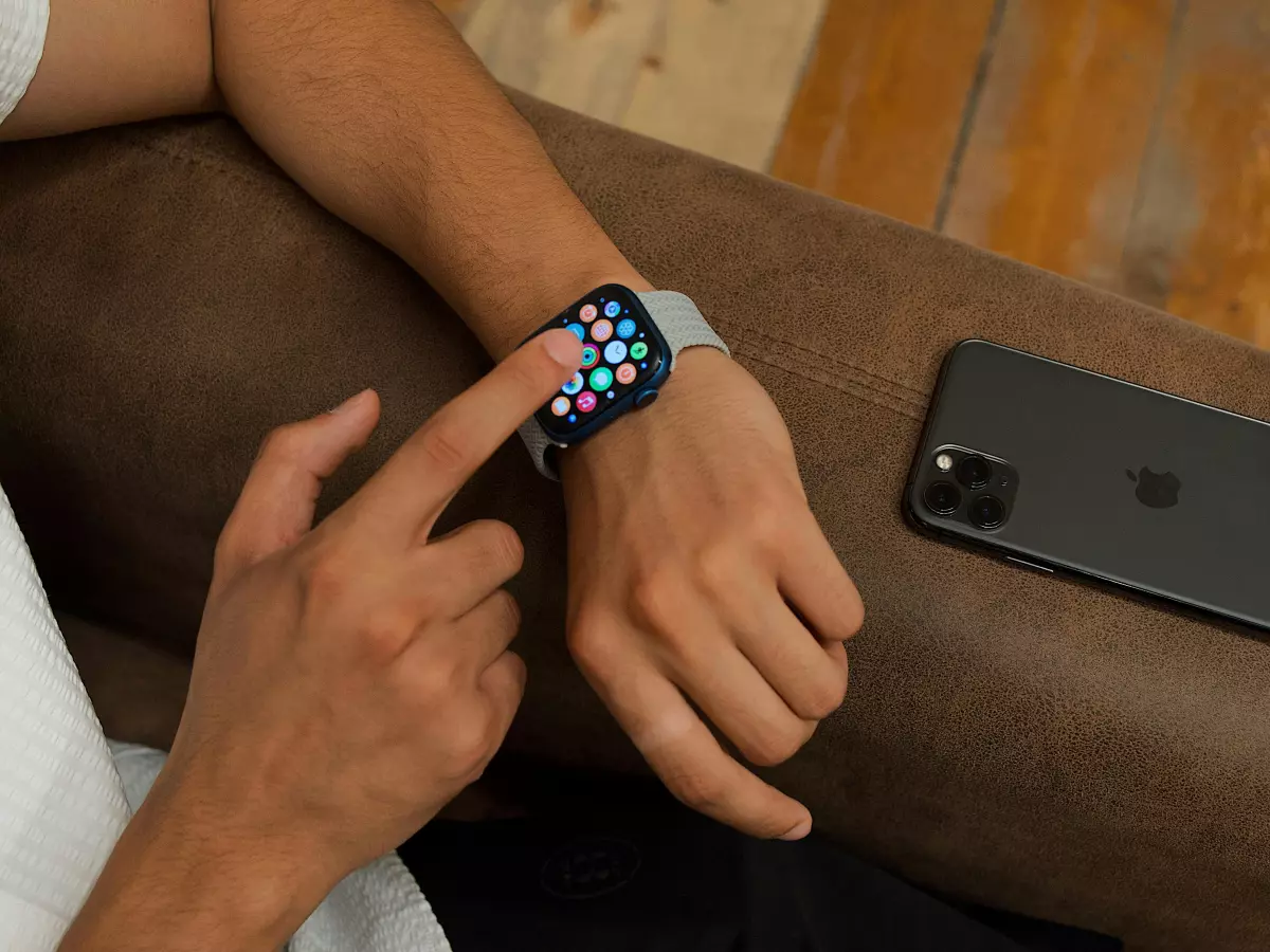 A person's hand is using the touch screen on an Apple Watch.  The watch is in focus and the background is blurred. The phone is out of focus in the background.