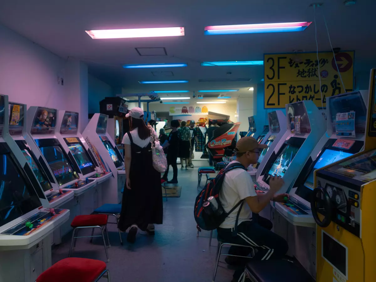 A row of arcade cabinets in a dimly lit room with people playing.