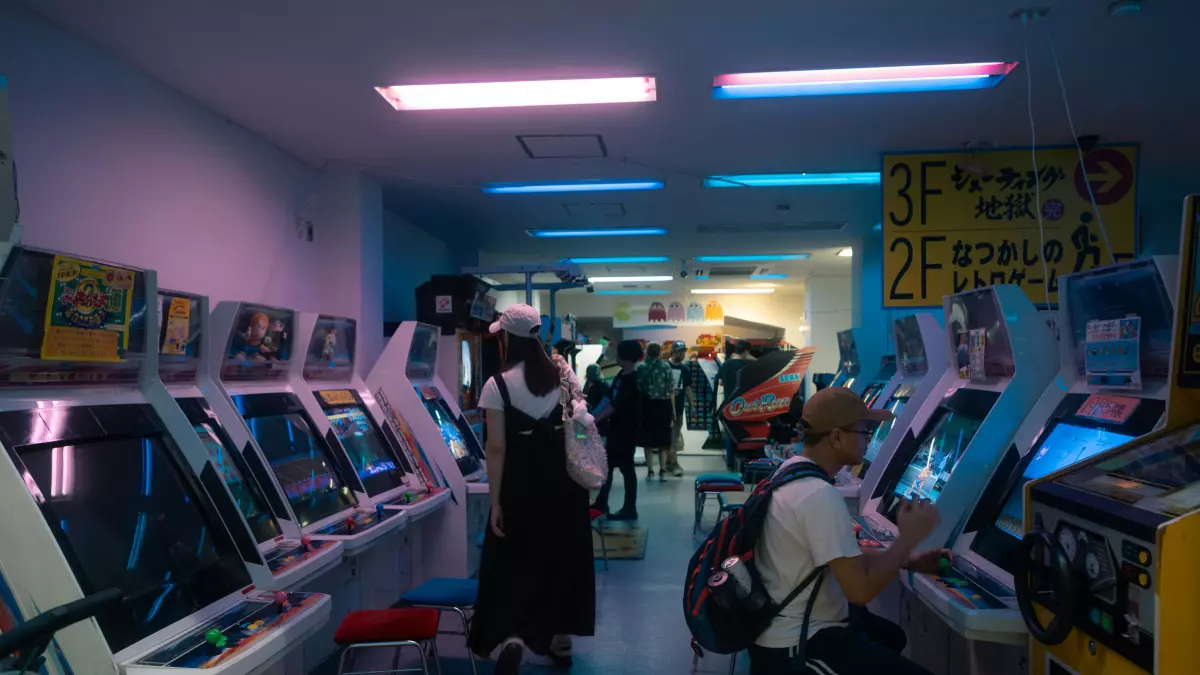 A row of arcade cabinets in a dimly lit room with people playing.