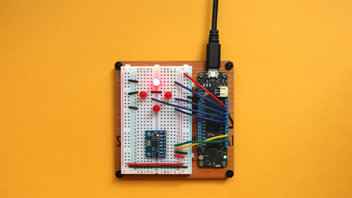 A close-up of a small circuit board with a microcontroller, LEDs, and a USB connector on a yellow background.