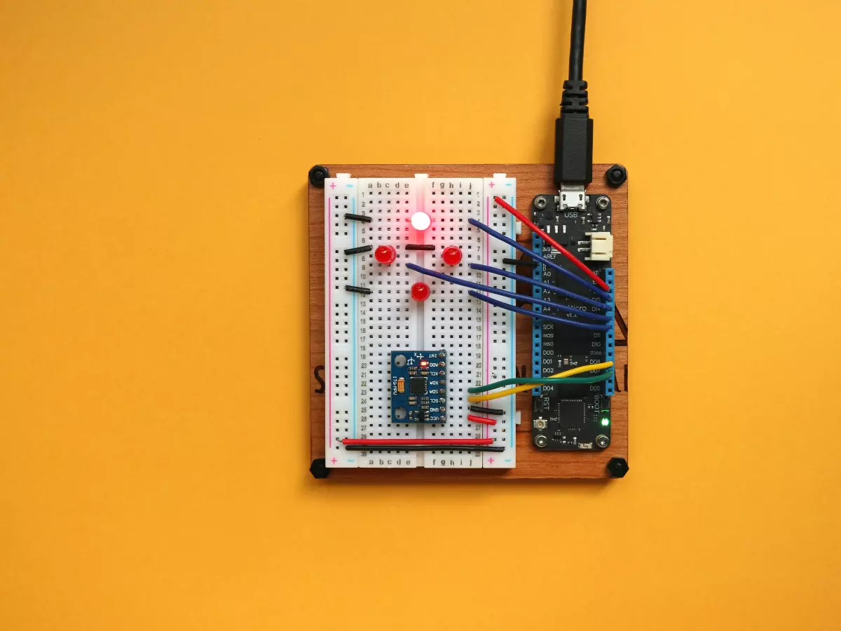 A close-up of a small circuit board with a microcontroller, LEDs, and a USB connector on a yellow background.