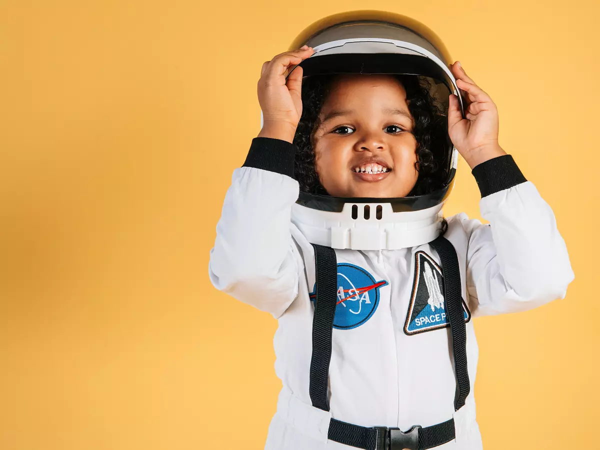 A child in an astronaut costume and helmet standing in front of a yellow background.