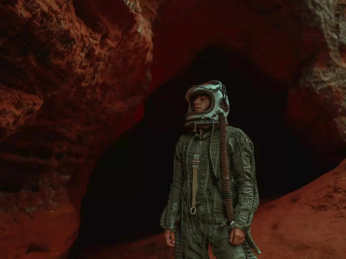 A person wearing an astronaut's helmet standing in a cave with red walls. 