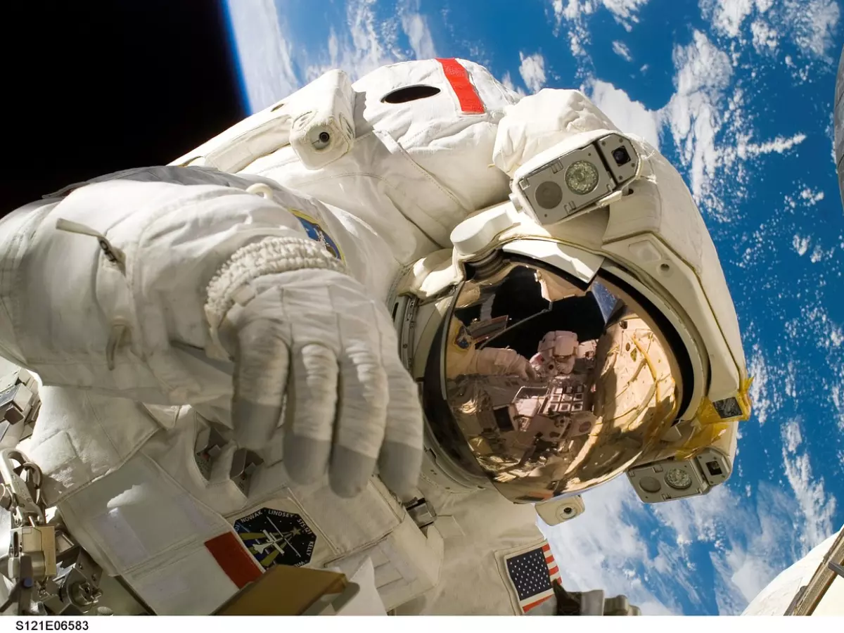 An astronaut in a white spacesuit, with a gold-tinted visor, looking out at the Earth from space.  