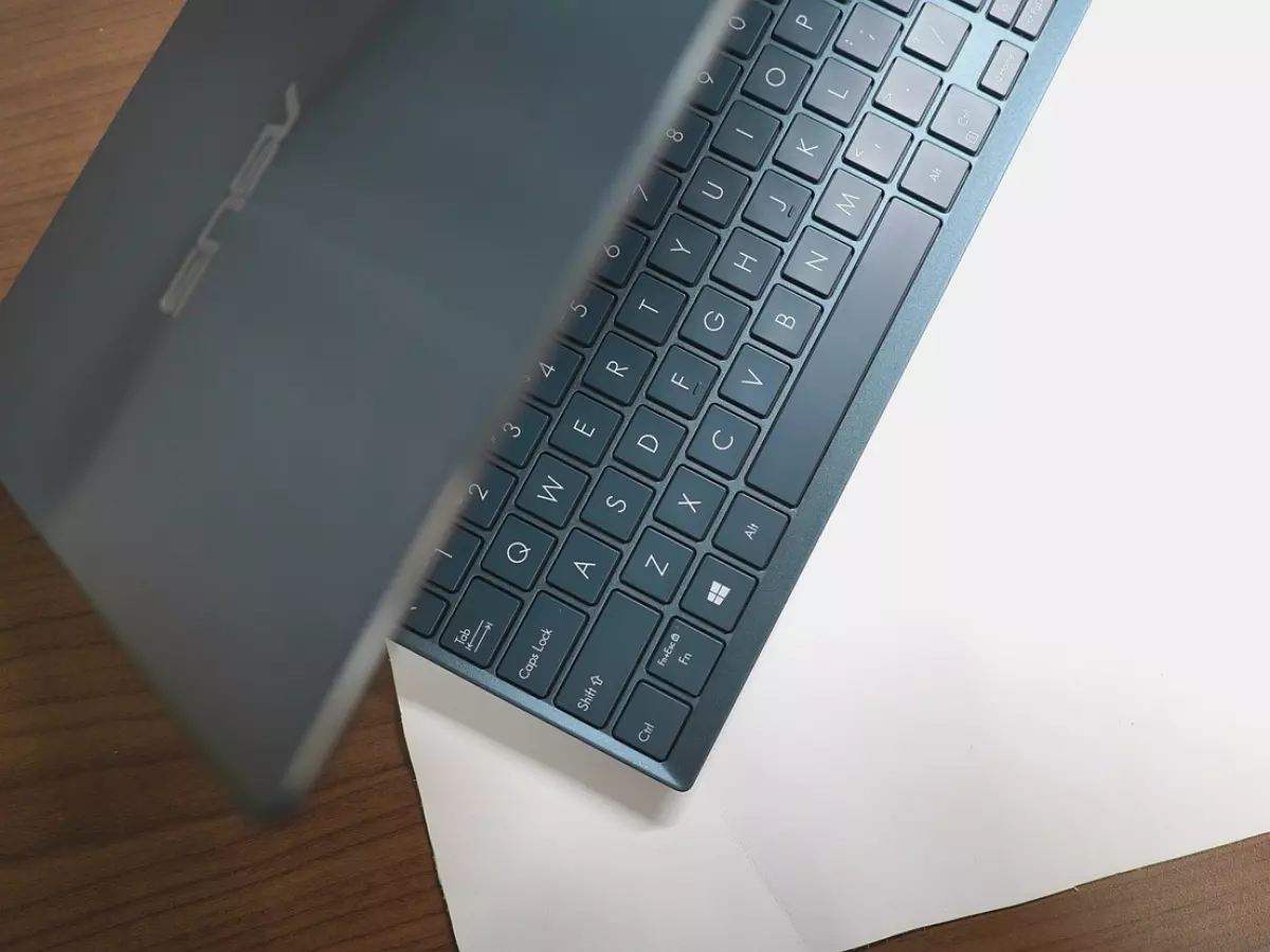 A person's hands are seen working on a laptop. The screen shows a video editing software with a dark background and blue and green elements.