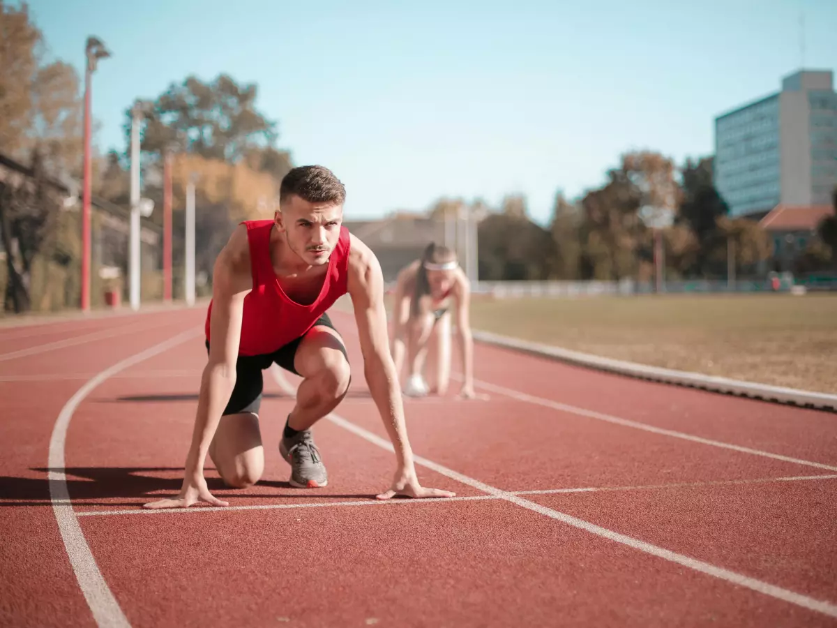 A runner is at the starting line of a track race, crouched and ready to spring forward.