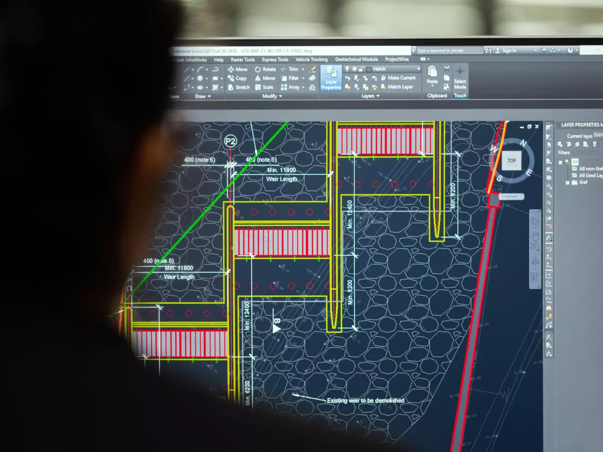 A person is looking at a computer screen with a technical diagram. The image is shot from behind the person, focusing on the screen. The colors are dark, with lines in red, yellow, and green.