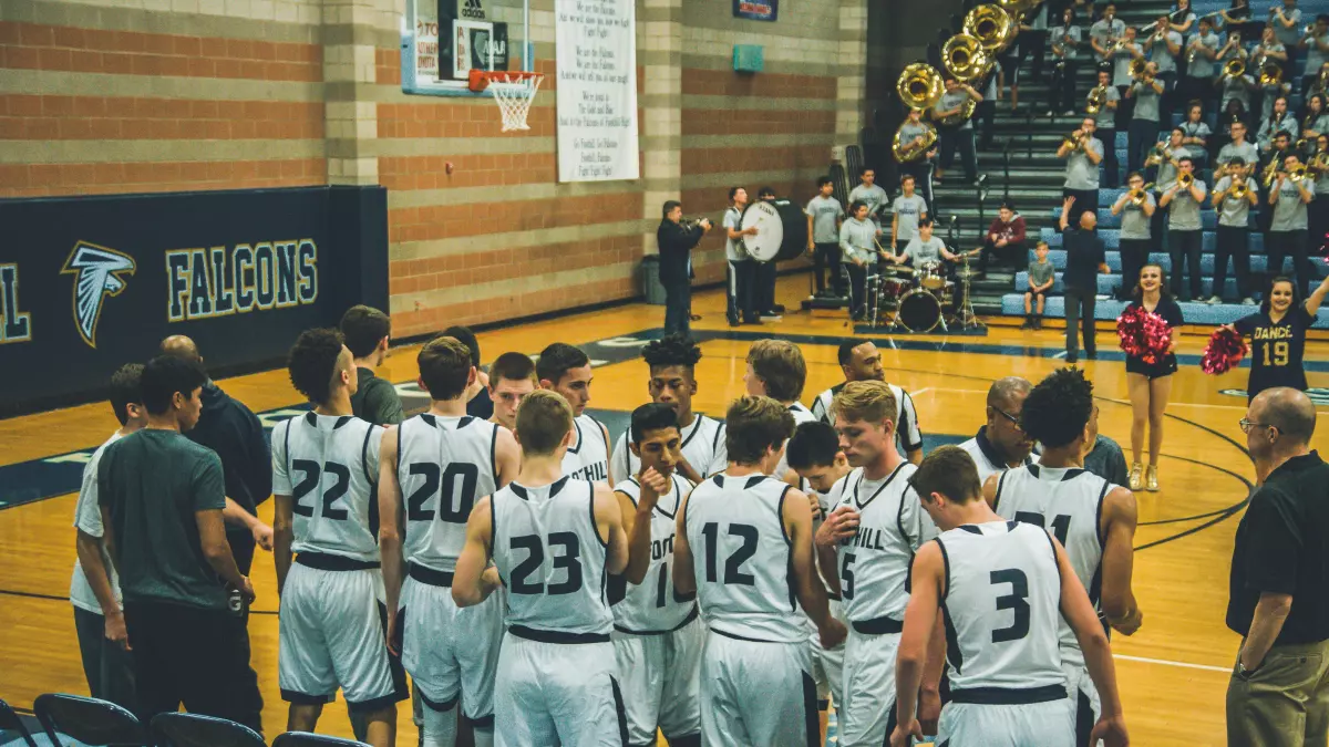 A basketball team huddles up in the middle of the court before a game.