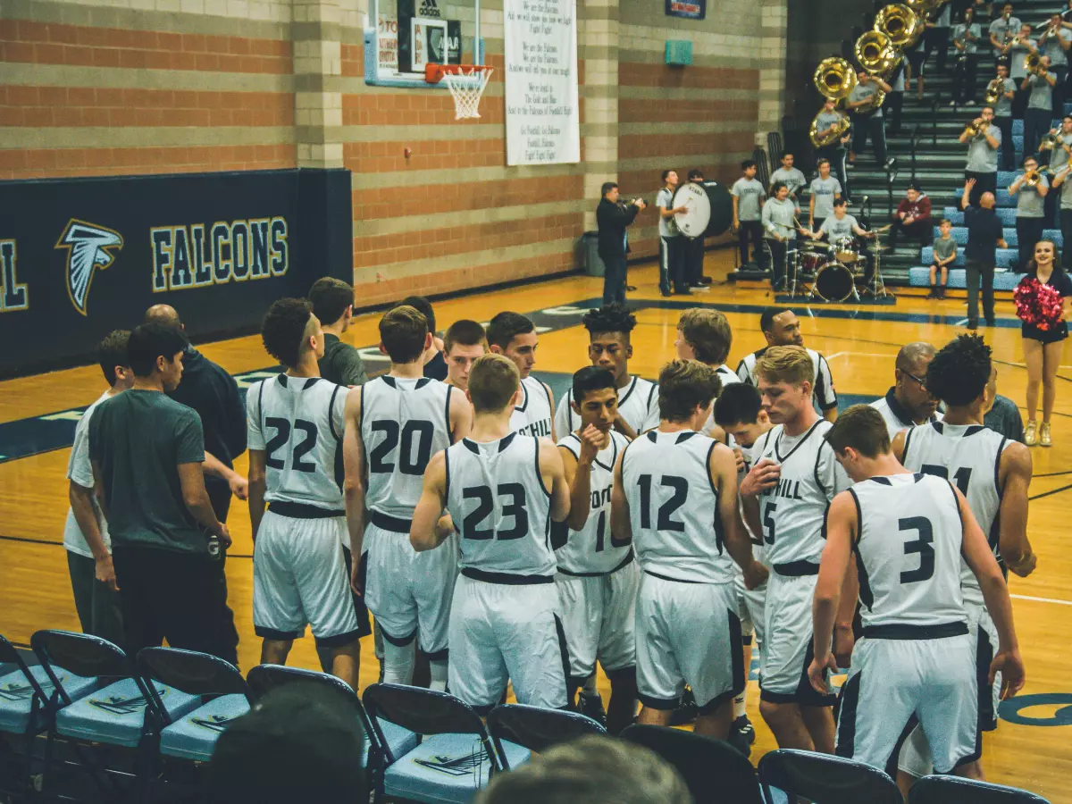 A basketball team huddles up in the middle of the court before a game.