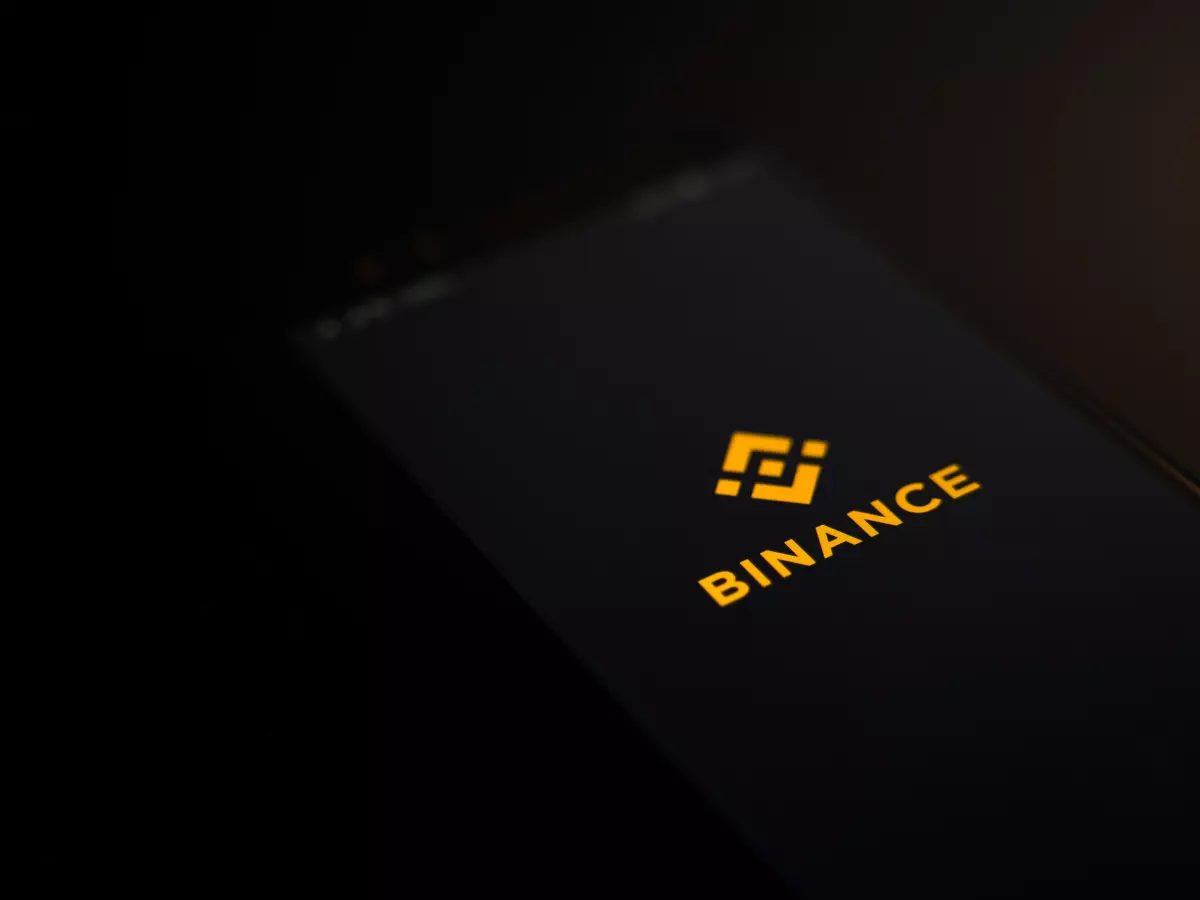 A black smartphone with the Binance logo displayed on the screen, shot from an angled perspective against a dark background.