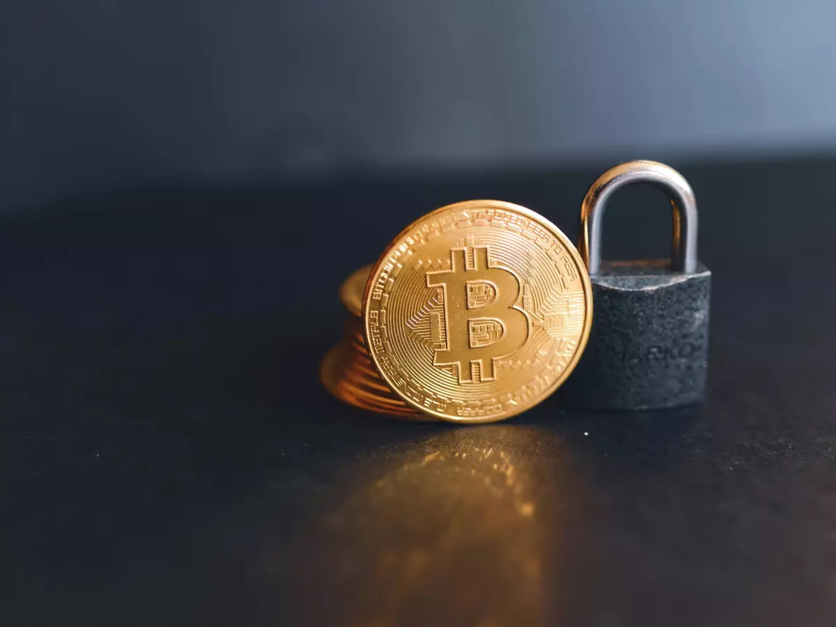 A gold Bitcoin coin is lying next to a closed padlock on a dark background. The image symbolizes security and protection.