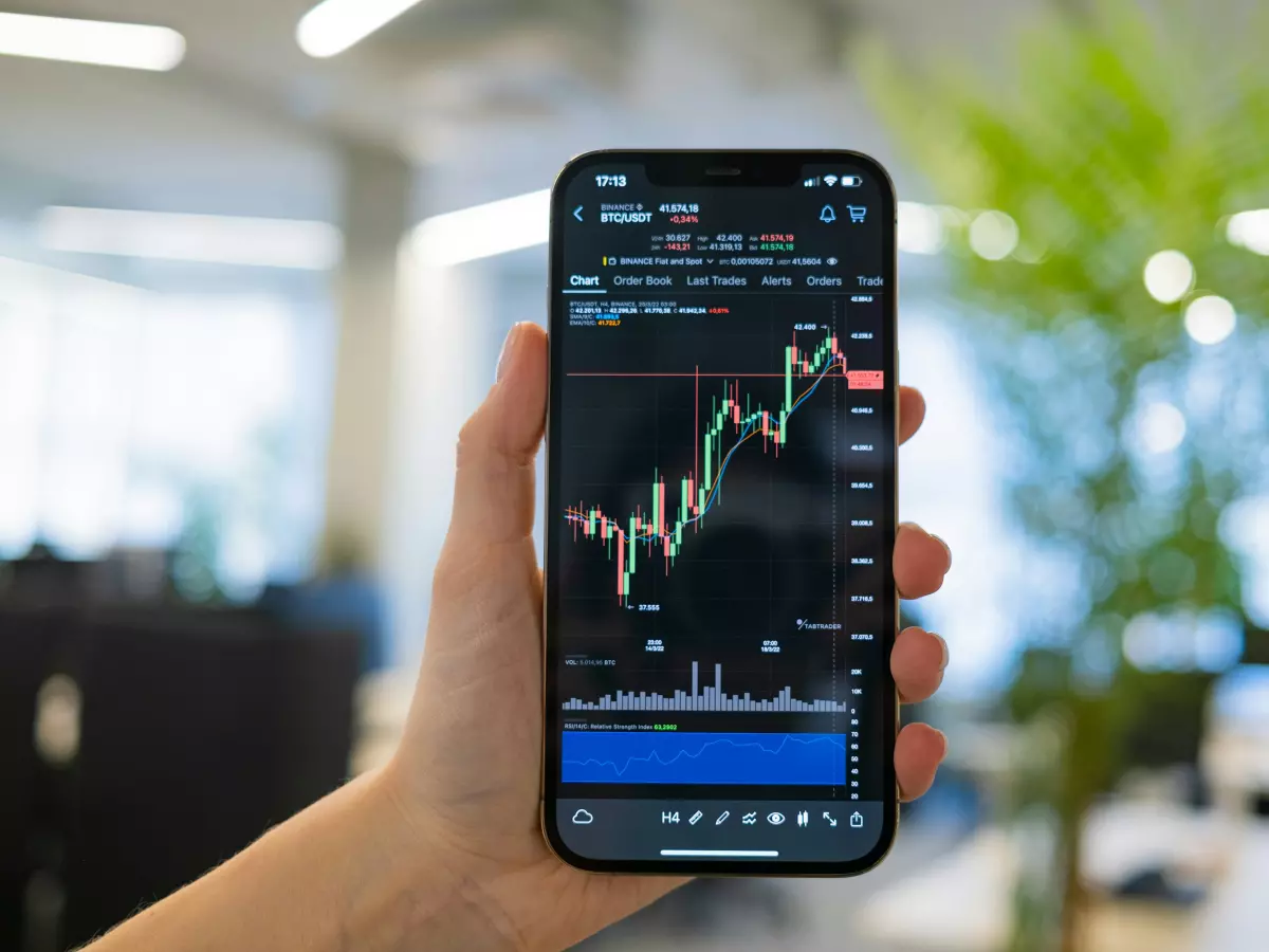 A hand holding a smartphone displaying a stock market chart with green and red lines