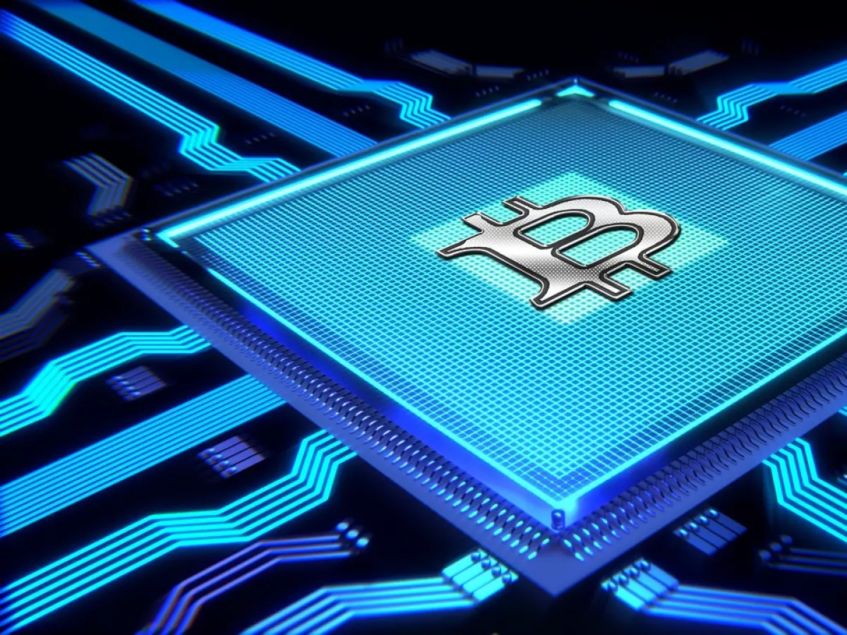 A 3D rendering of a bitcoin symbol in a circuit board. The symbol is silver and is glowing in the center of a blue circuit board, surrounded by a dark background.