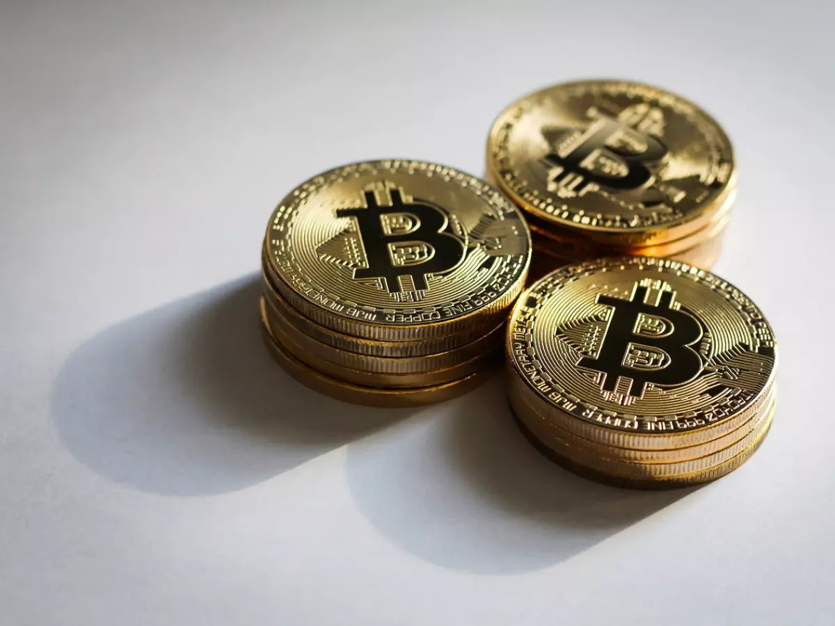 Three stacks of golden Bitcoin coins on a white surface. They are arranged in a triangle formation with some shadowing around them.