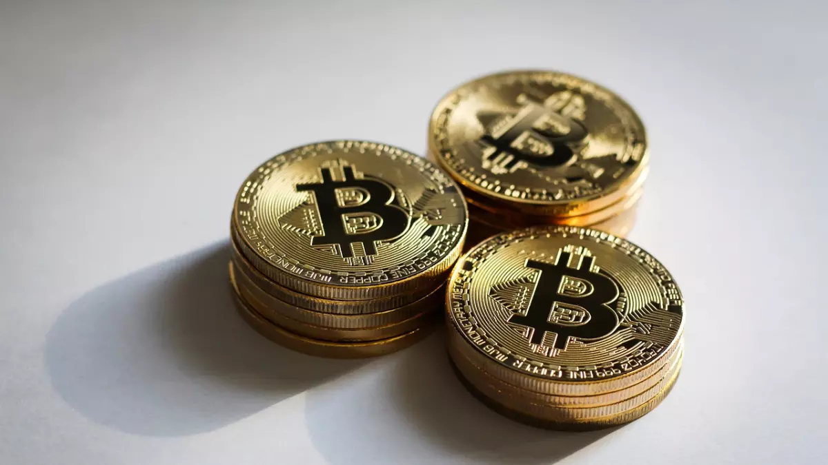 Three stacks of golden Bitcoin coins on a white surface. They are arranged in a triangle formation with some shadowing around them.