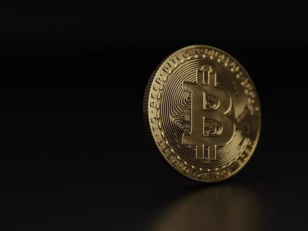 A gold-colored Bitcoin coin lying on a black surface.