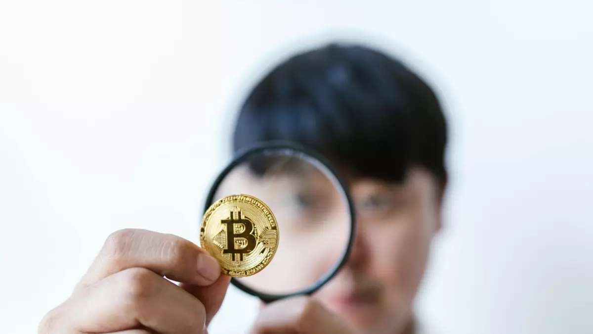 A close-up shot of a hand holding a Bitcoin coin with a magnifying glass in front of it.