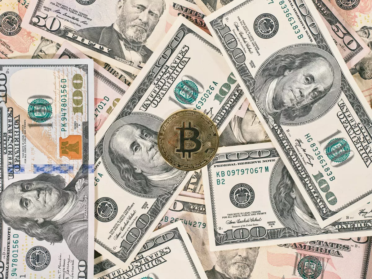 A Bitcoin coin sits on top of a pile of US dollar bills, highlighting the merging of traditional and digital currencies.