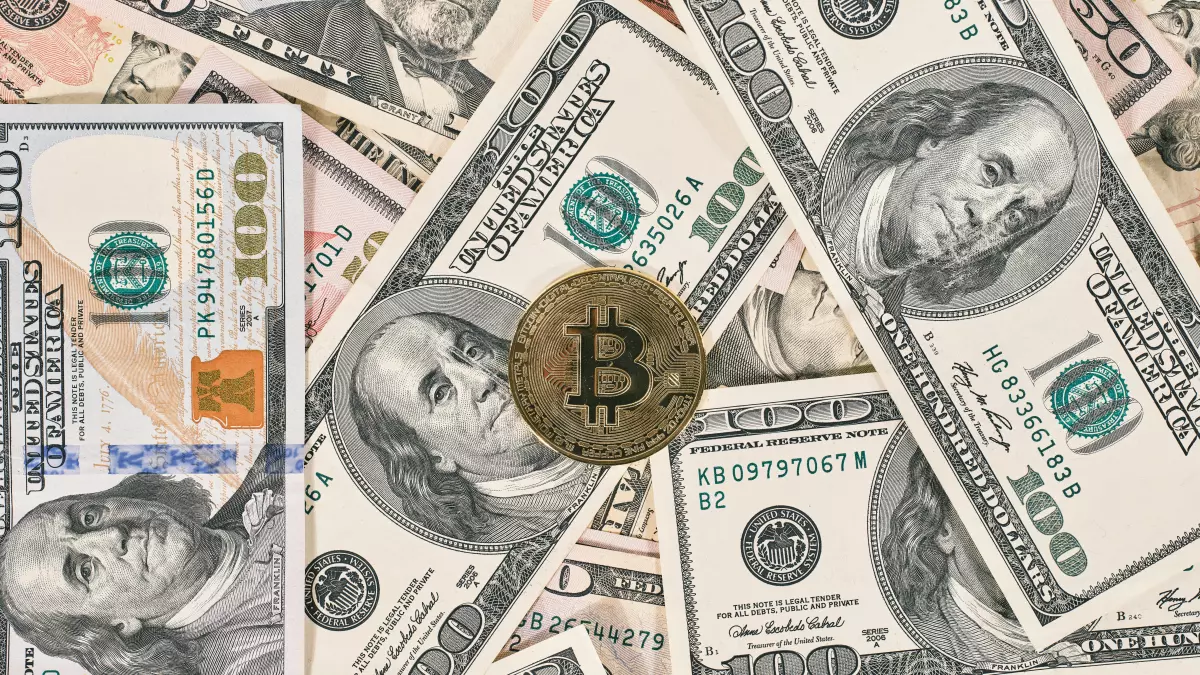 A Bitcoin coin sits on top of a pile of US dollar bills, highlighting the merging of traditional and digital currencies.