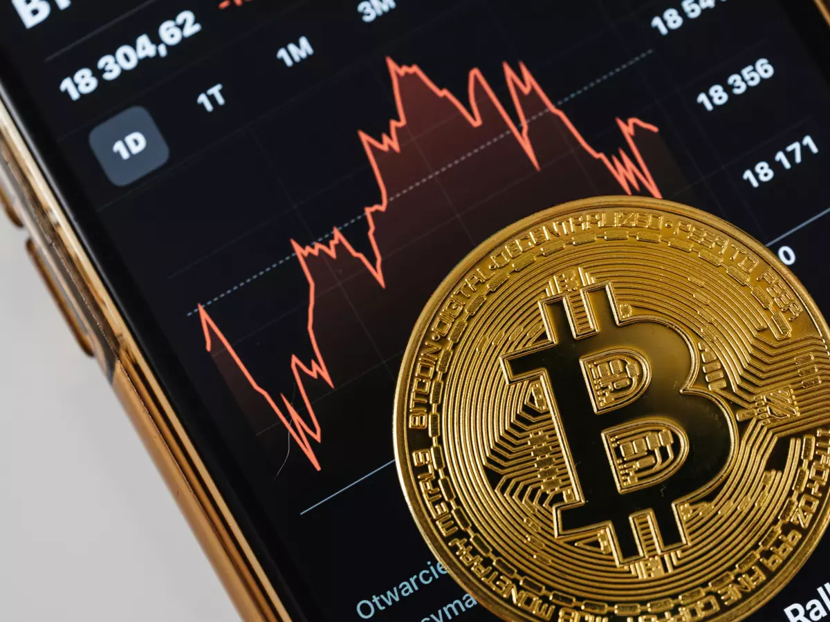 A gold Bitcoin coin resting on a smartphone displaying a cryptocurrency price chart.