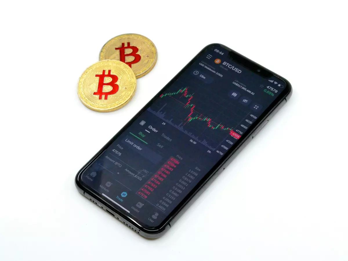 A smartphone displaying a Bitcoin chart alongside two gold Bitcoin coins.