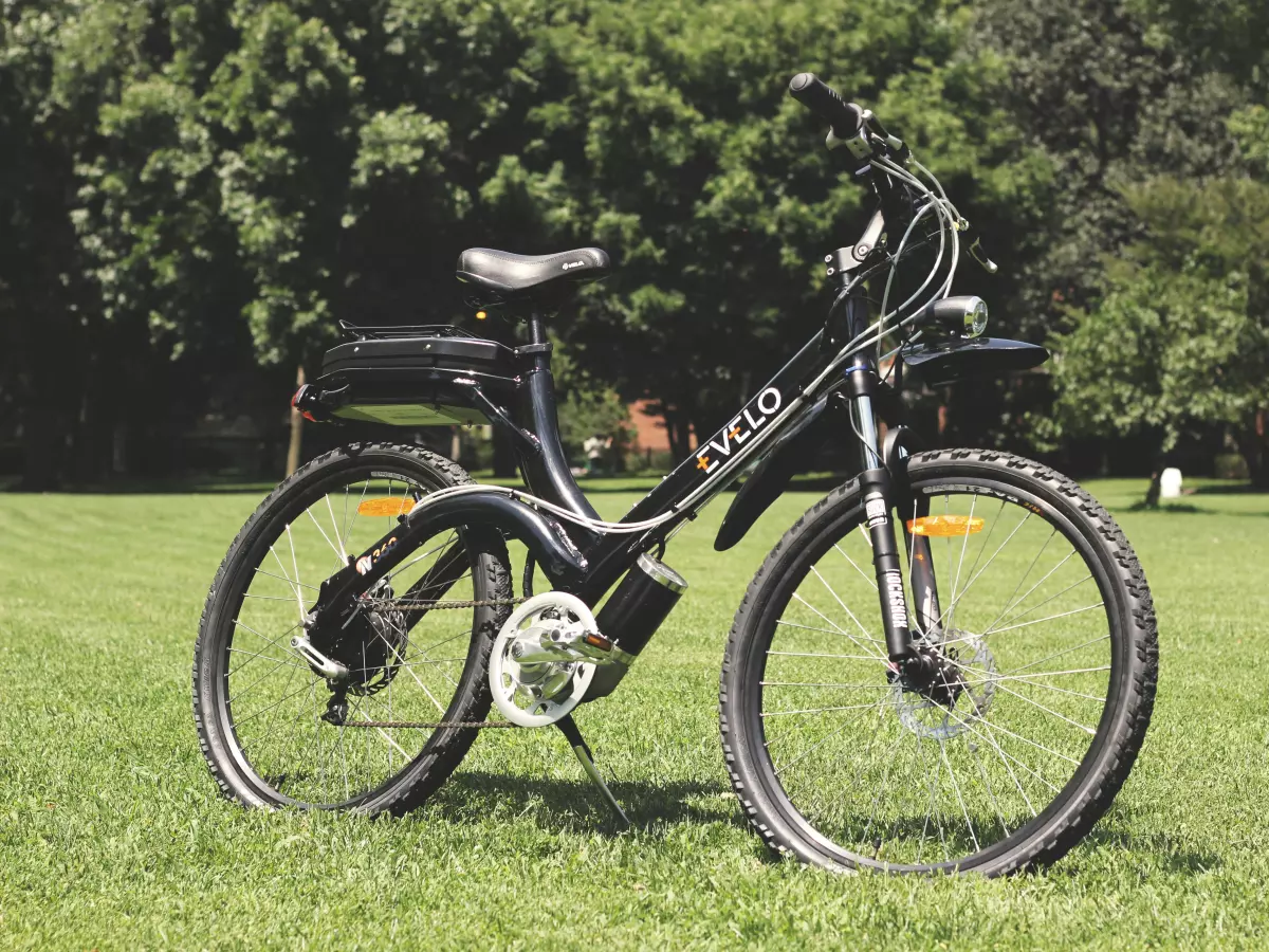 A black electric bicycle with a battery on the back frame, standing on a grassy field.