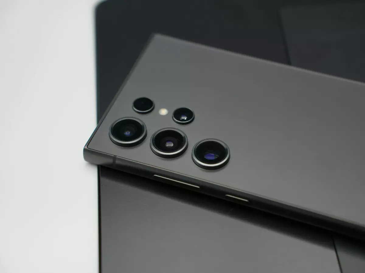 A close-up shot of the back of a Samsung Galaxy Quantum 5 smartphone, focusing on its camera system. The phone is black and lies on a grey surface.