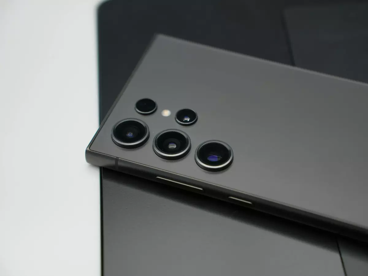 A close-up of a sleek black smartphone lying on a white surface, showcasing its design and camera setup.