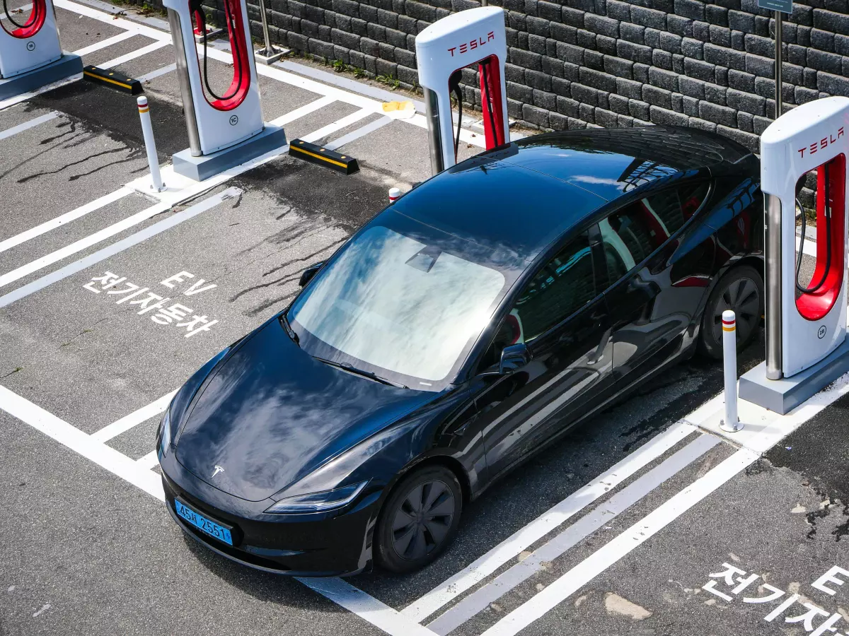 A Tesla Model 3 is charging at a charging station with the charging cable plugged in. The car is parked in a designated charging spot, with a sign indicating that it is reserved for EV charging. The charging station has two charging ports, and the car is connected to one of them.