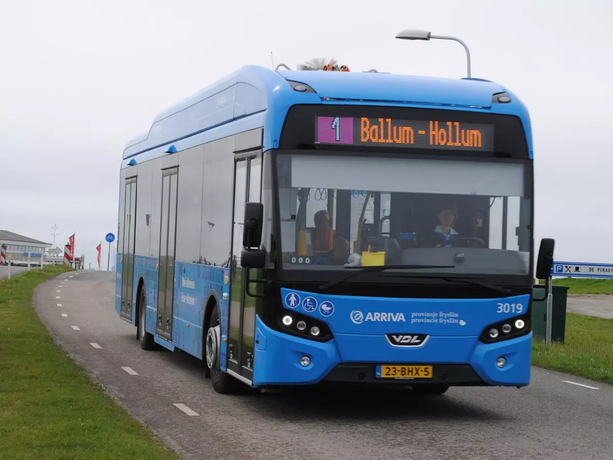 A blue electric bus driving on a road, with a sign on the front that says "Ballum-Hollum".