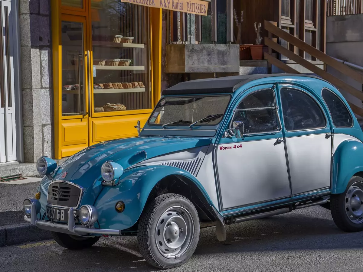 A vintage blue and white car with a yellow storefront in the background.