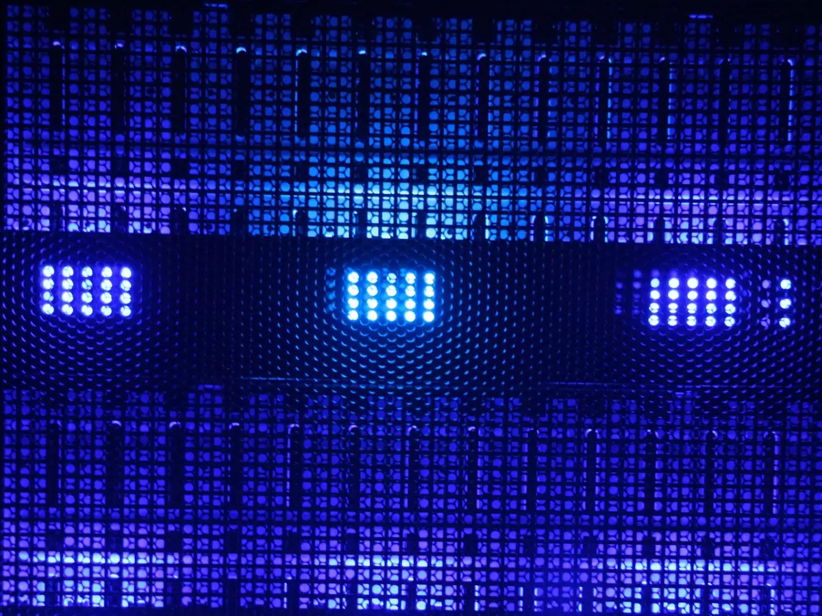 A close-up shot of a server rack with blue and purple lighting. The rack is made of metal and has a honeycomb pattern. The lighting illuminates the rack from the front, creating a dramatic effect.