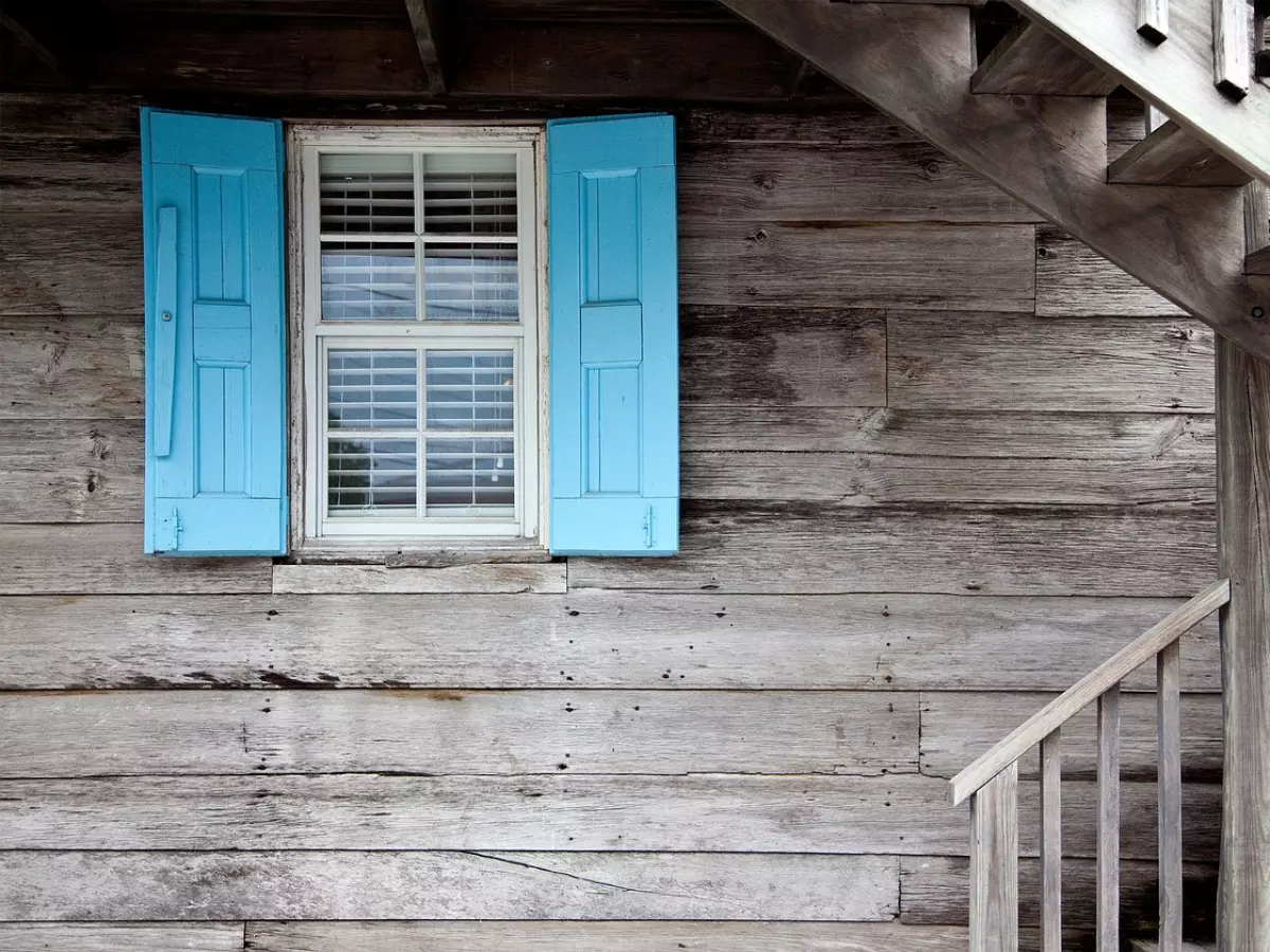 A wooden house with blue shutters and a staircase, the image is taken from the outside.