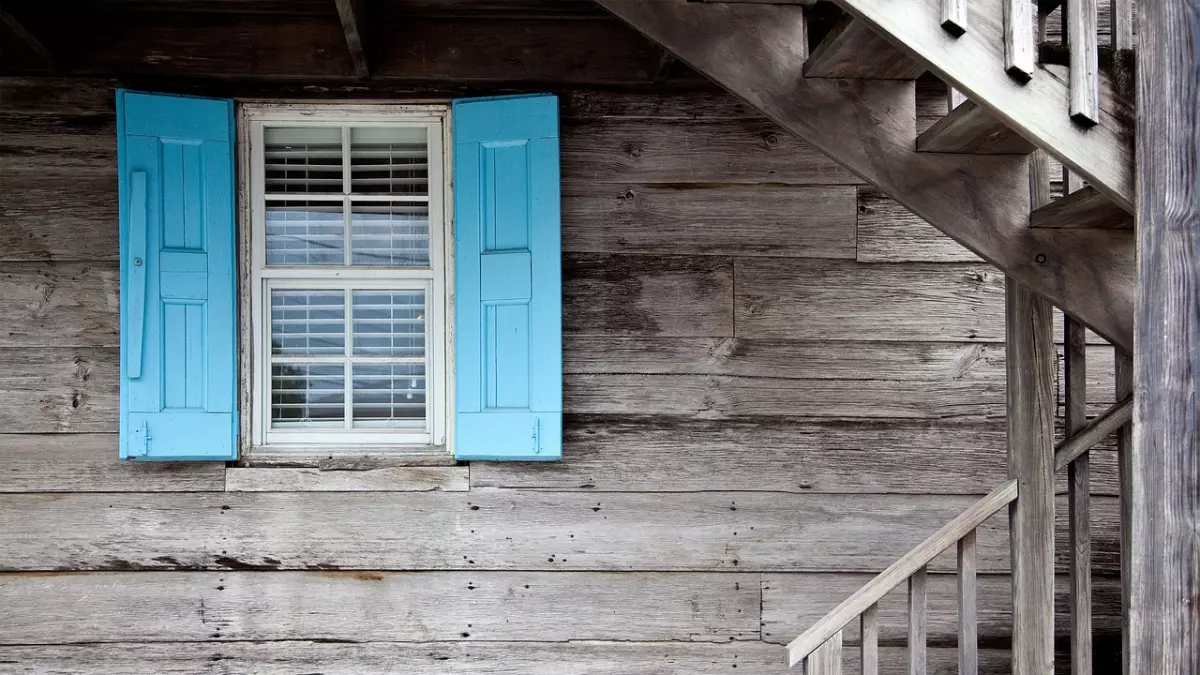 A wooden house with blue shutters and a staircase, the image is taken from the outside.