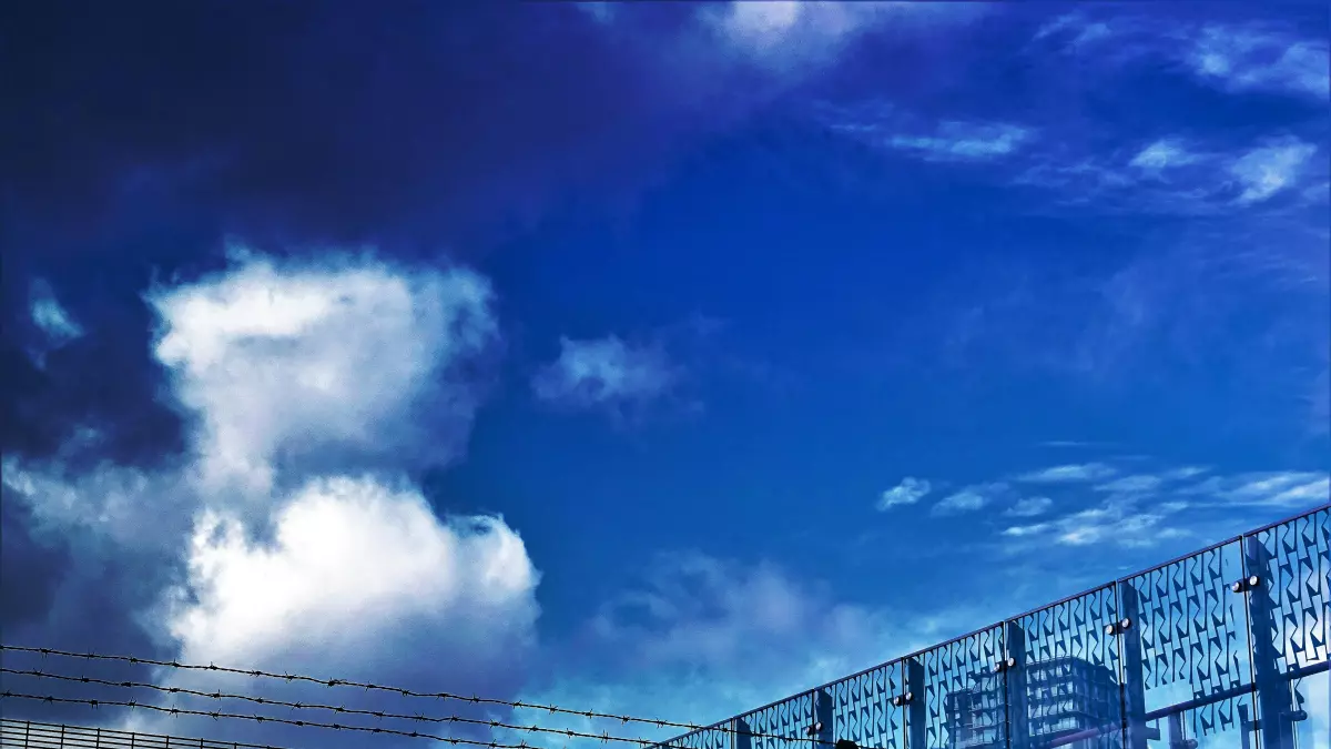 A view of a fence in front of a city skyline under a cloudy sky.