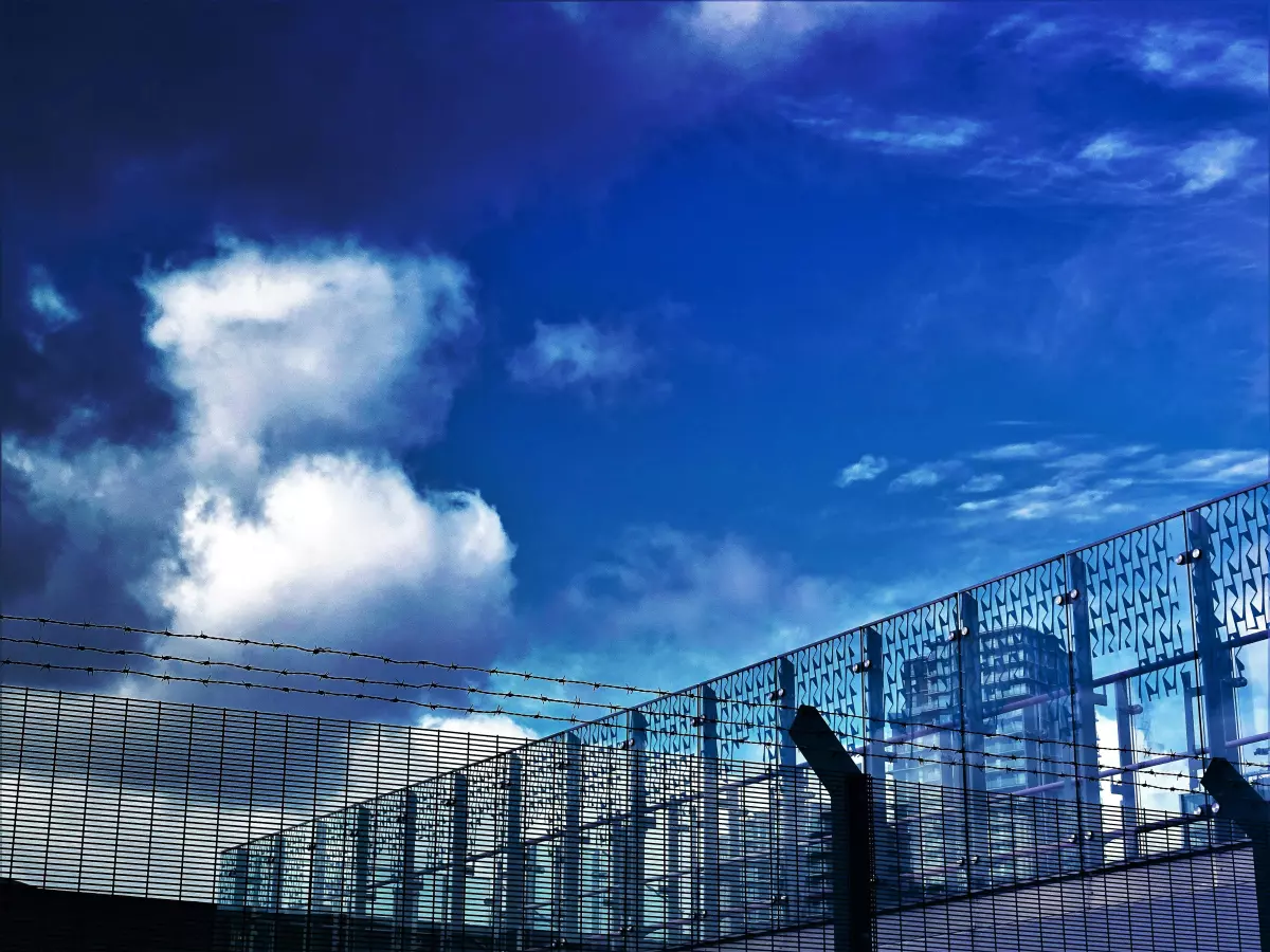 A view of a fence in front of a city skyline under a cloudy sky.