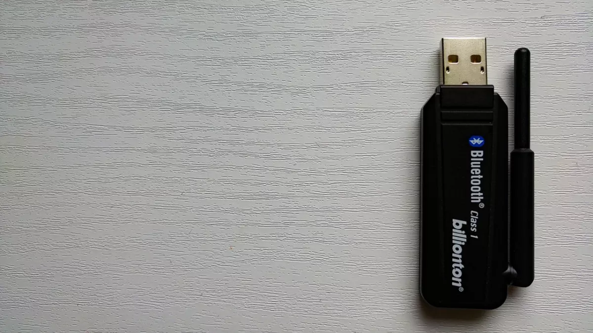 A black USB Bluetooth adapter with a small antenna on a white wooden surface.