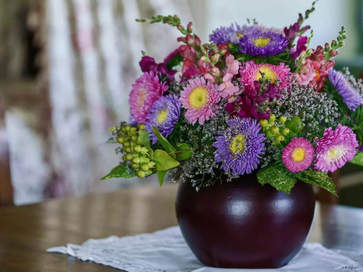 A flower arrangement in a dark purple vase on a table with a white tablecloth.