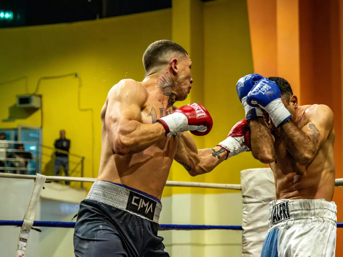 Two boxers fighting in a ring, the man in blue is on the right side of the image, the man in red is on the left side of the image, the man in blue throws a punch with his right hand.